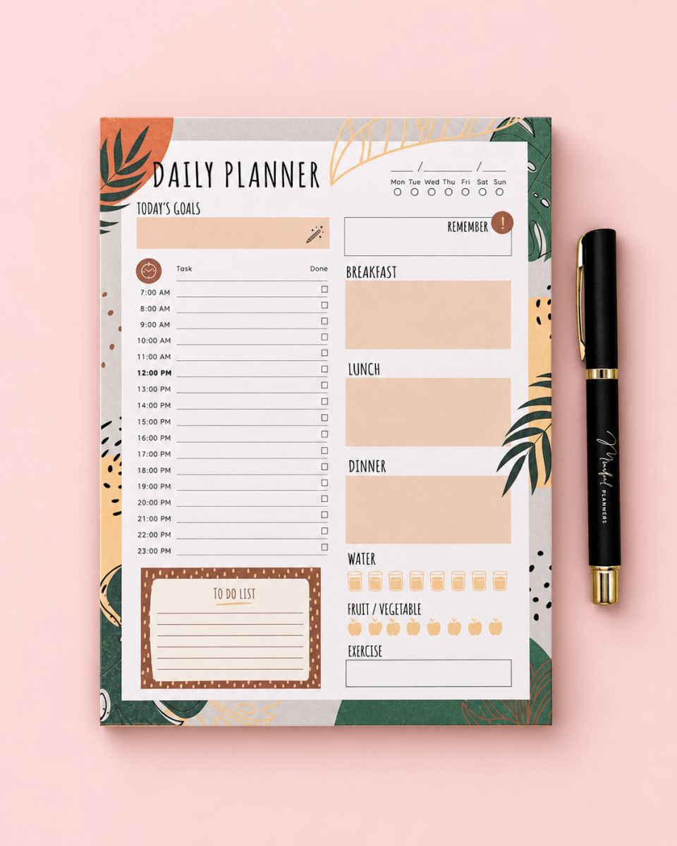 A daily planner pad with a botanical and geometric patterned cover, shown flat on a light pink background next to a black pen with gold trim.