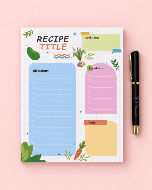 A recipe planner notepad with a grid background and colorful illustrated sections for title, directions, ingredients, cook time, and notes, shown on a pink background next to a black pen with gold trim.