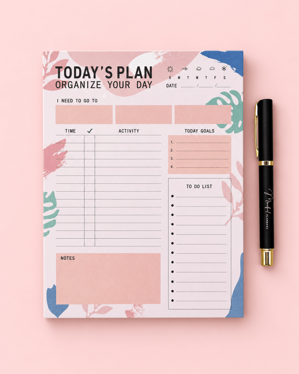 A pastel-colored daily planner notepad with a matching black and gold pen, styled flat-lay on a solid pink background.