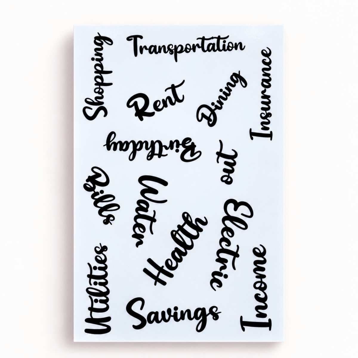 A rectangular white canvas wall art print featuring black cursive script words like Transportation, Shopping, Rent, Dining, Insurance, Utilities, Water, Health, Savings, and Income, shown against a light gray background.